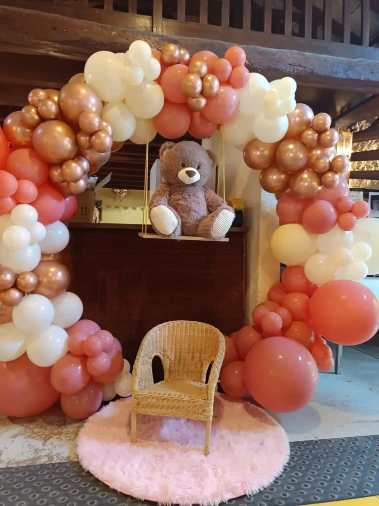 Arche de ballons rose, blanc et or rose avec ours en peluche sur balançoire pour dĂ©coration dâanniversaire enfant.