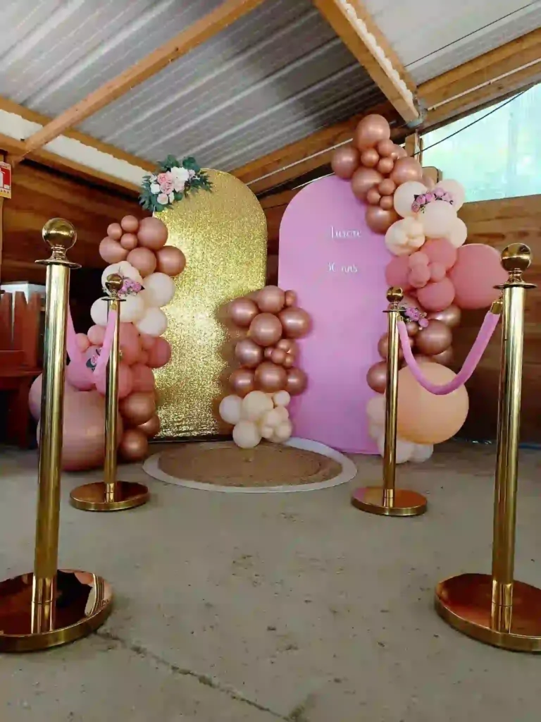 Arche de ballons rose, blanc et or devant panneaux pailletes or et rose, espace photocall avec potelets dorés.
